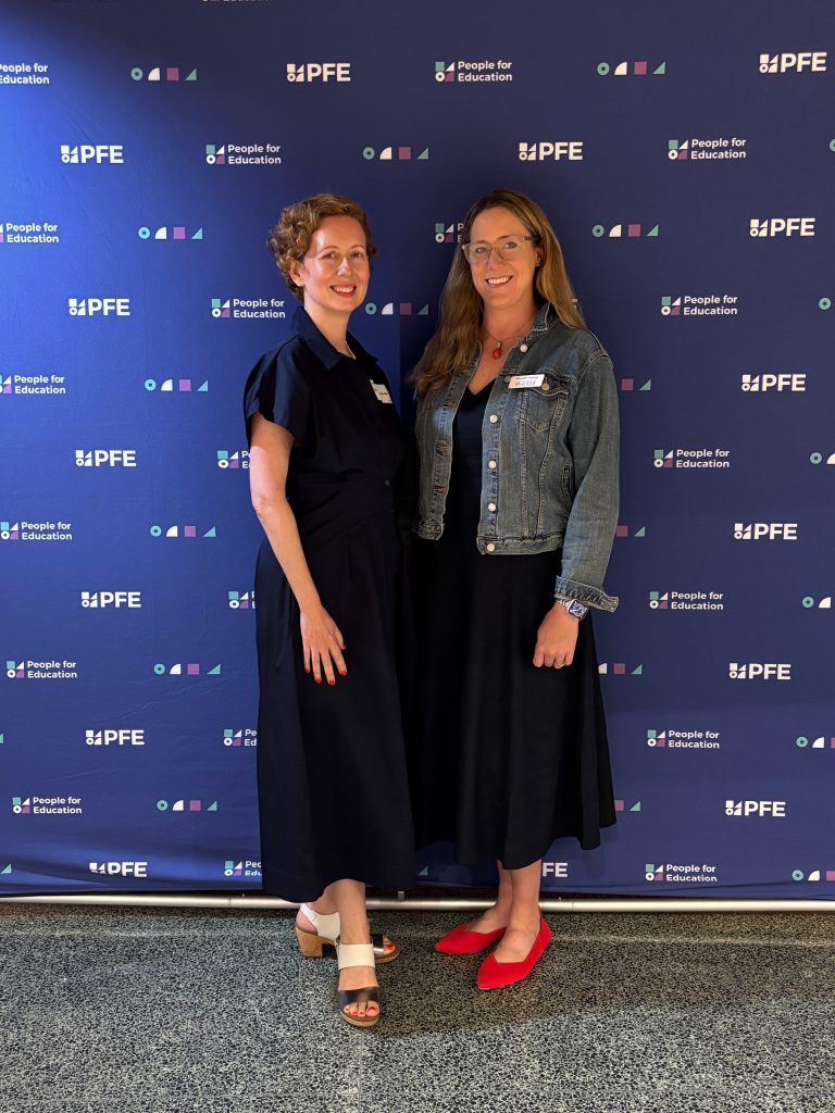Two people standing in front of a People for Education media wall.